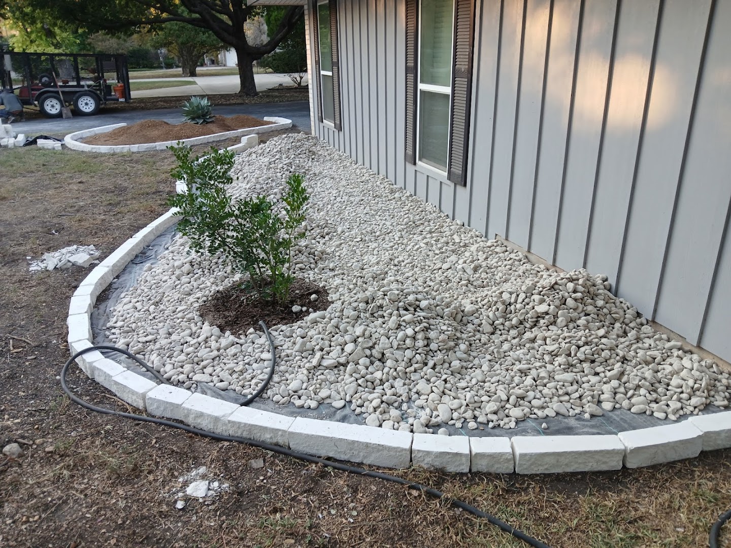 River rock landscape bed with stone border and tree, Seguin TX